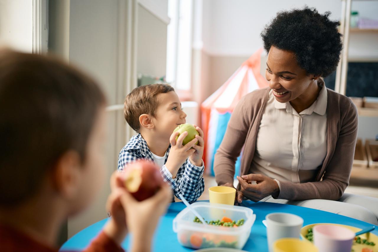 A teacher sitting with children eating lunch