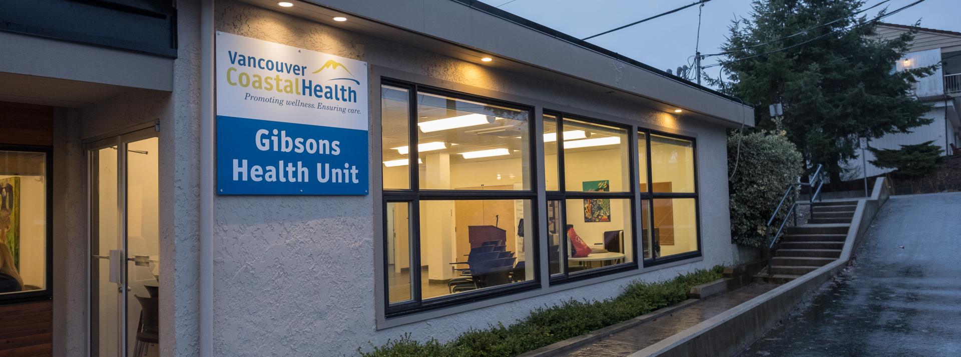 Exterior shot of Gibsons Health Unit at dusk. The lights are on inside and the sign is visible on the outside.