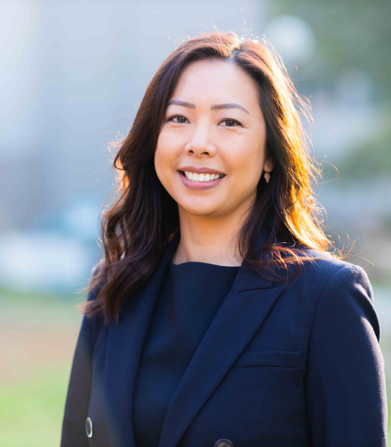 A portrait for Charlene Chiang outside on a sunny day. She is wearing a dark blue blazer.