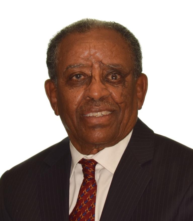 A portrait of Eyob Goitom Naizghi in front of a white background. He is wearing a red tie and dark suit