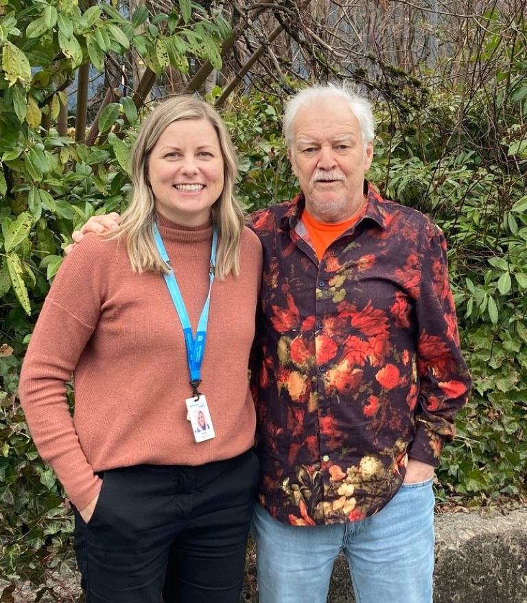 Heidi Butler and D'Arcy McCrea pose for a photo in front of a hedge