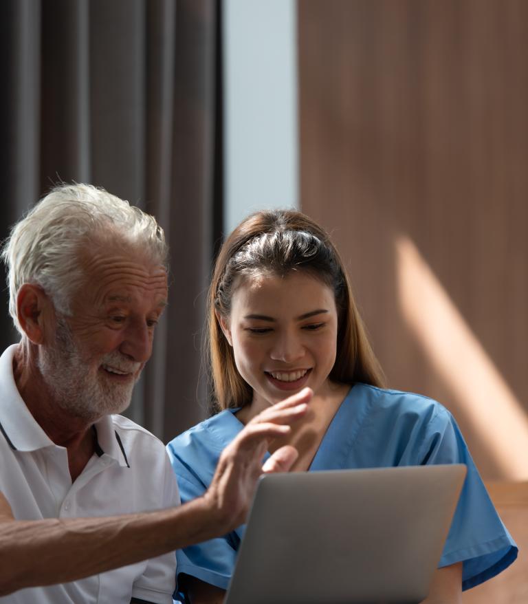 A nurse smiling while she views a laptop with an older patient