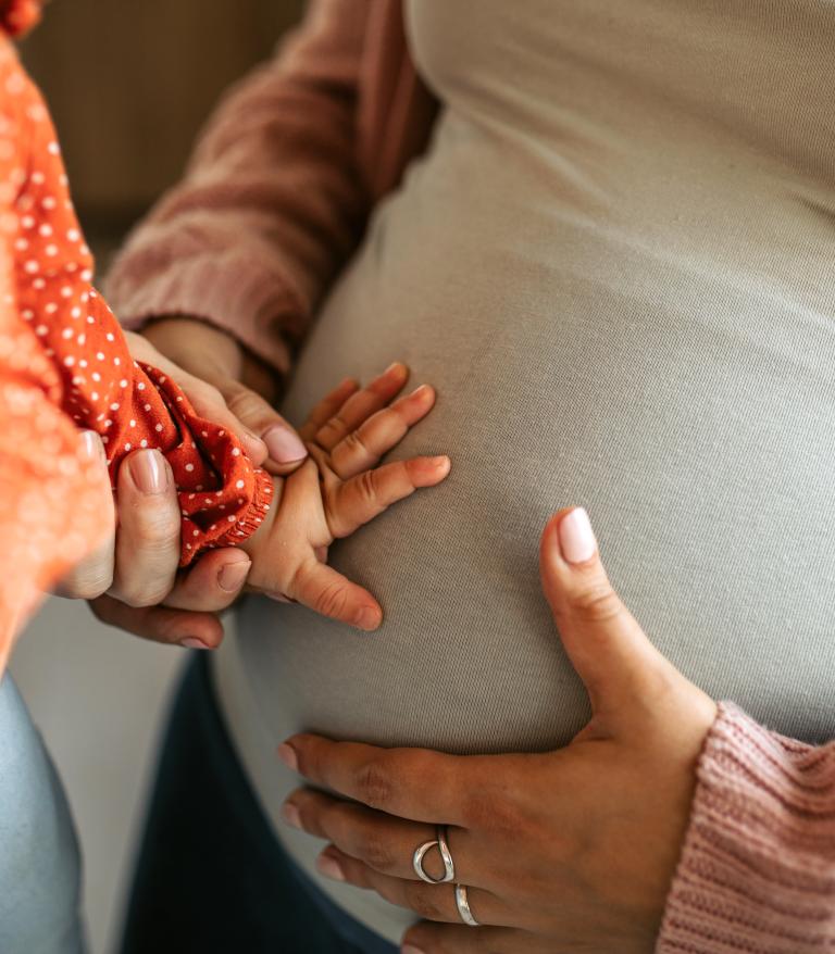 Closeup of a childs hand resting on a pregnant mothers stomach